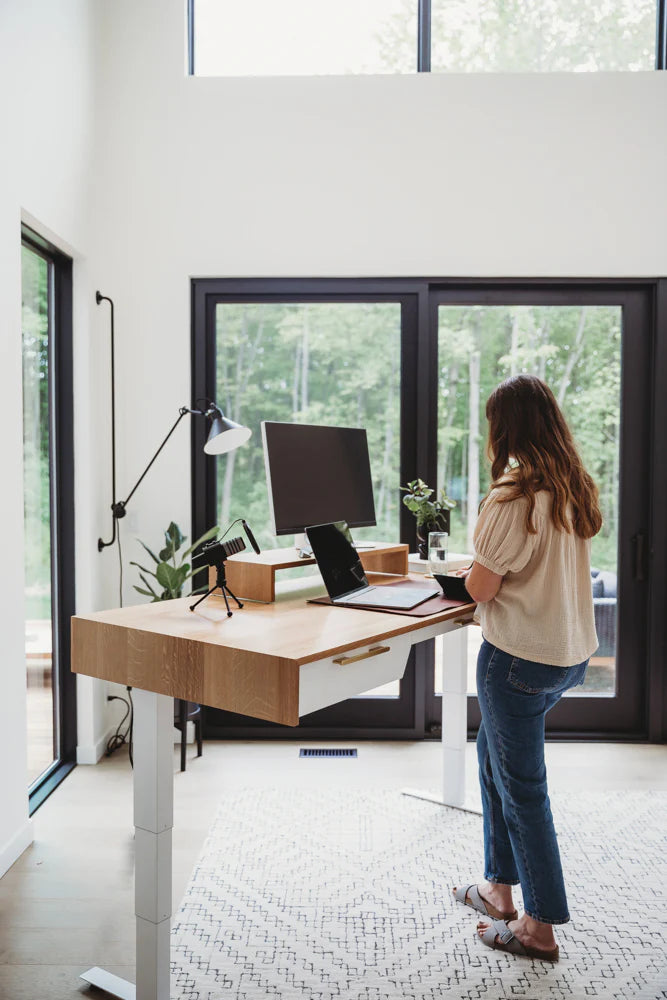 Hight adjustable standing desk, with big monitor and laptop on it, and woman working in a cozy environment 